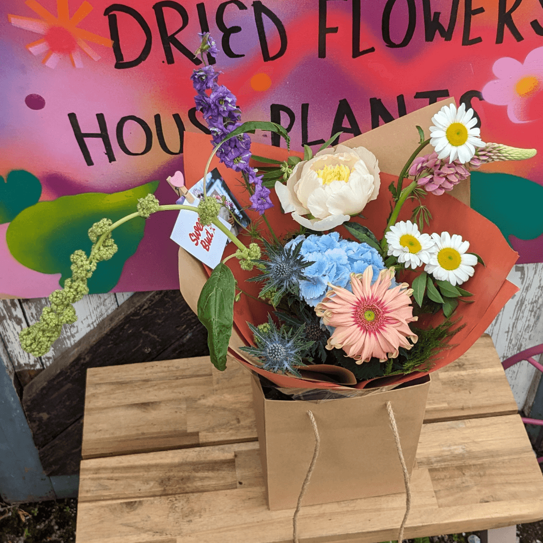 pastel and bright flowers in a bouquet with orange paper wrap and a blue hydrangea